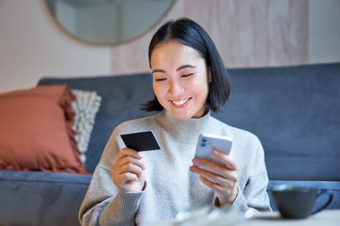 Portrait of smiling asian woman paying with credit card on her smartphone app, arrange direct debit or shopping online from mobile phone